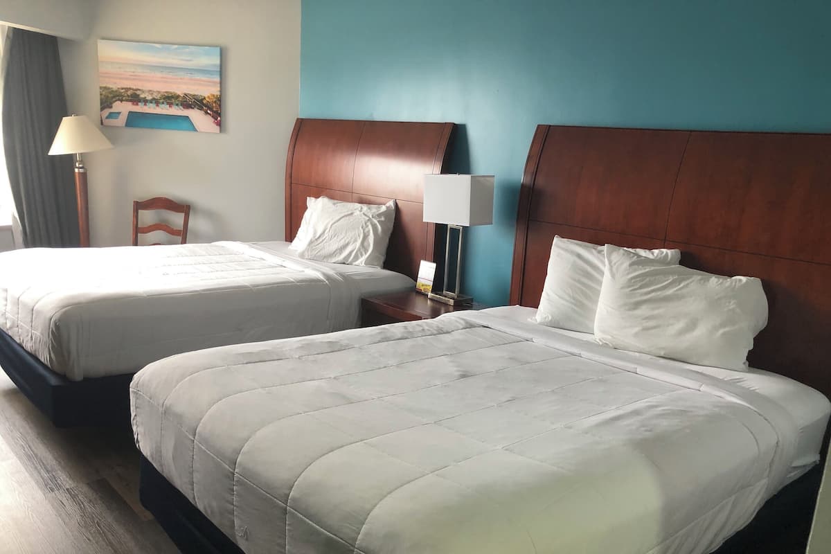A hotel room with two beds, a nightstand, a lamp, and a painting of a beach scene.