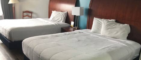 A hotel room with two beds, a nightstand, a lamp, and a painting of a beach scene.
