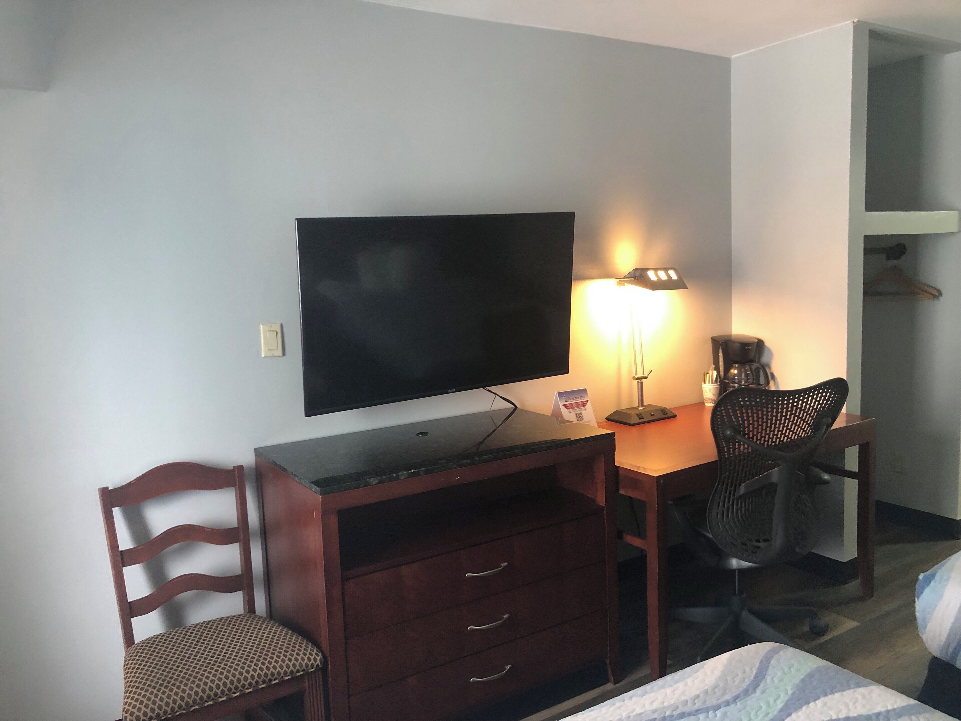 Ett hotellrum med en platt-TV, ett skrivbord med en lampa, en stol, en säng och en garderob.