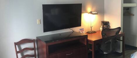 Ett hotellrum med en platt-TV, ett skrivbord med en lampa, en stol, en säng och en garderob.