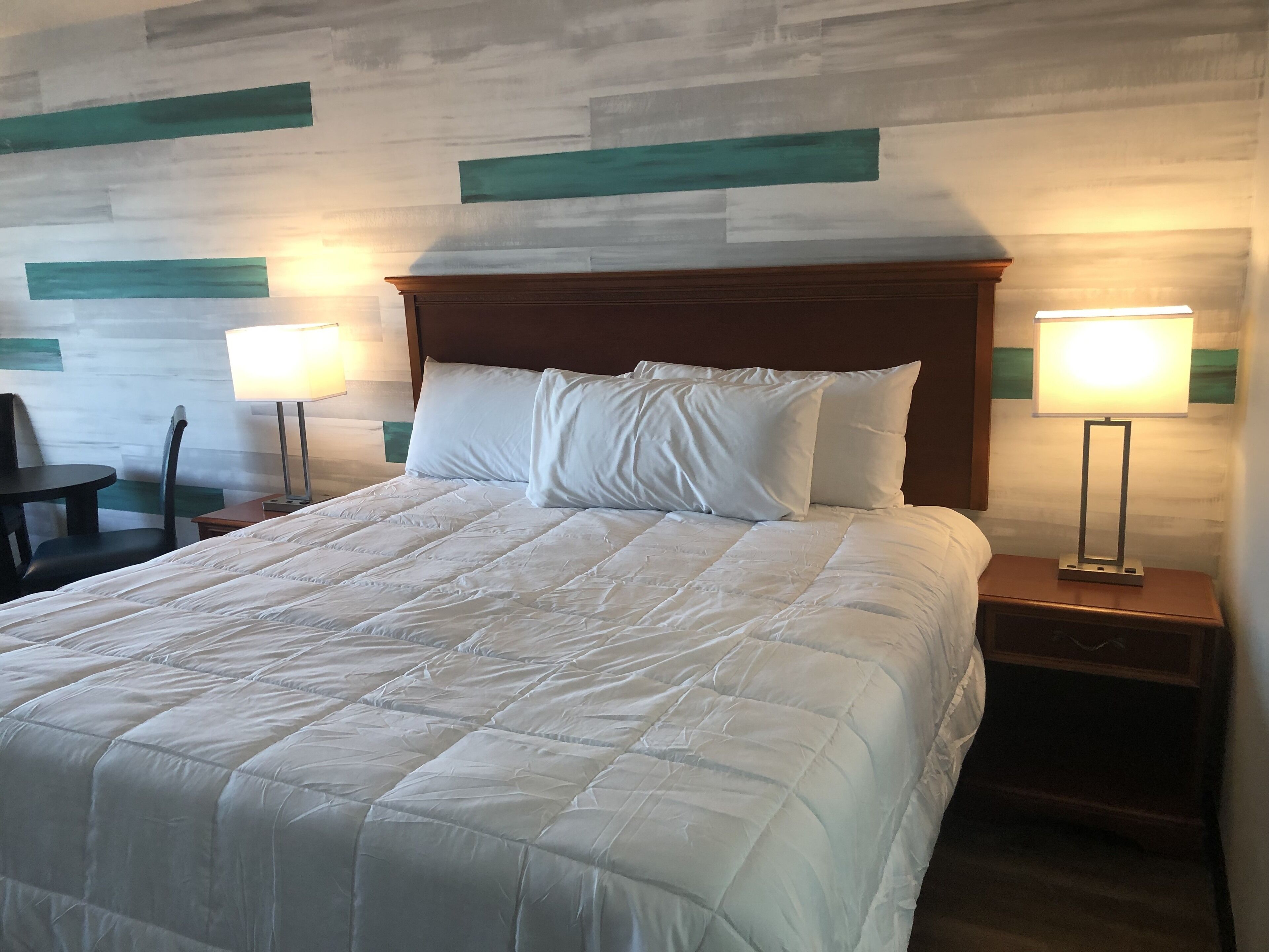 Una cama bien hecha con ropa blanca, cabecera de madera y dos lámparas de noche.