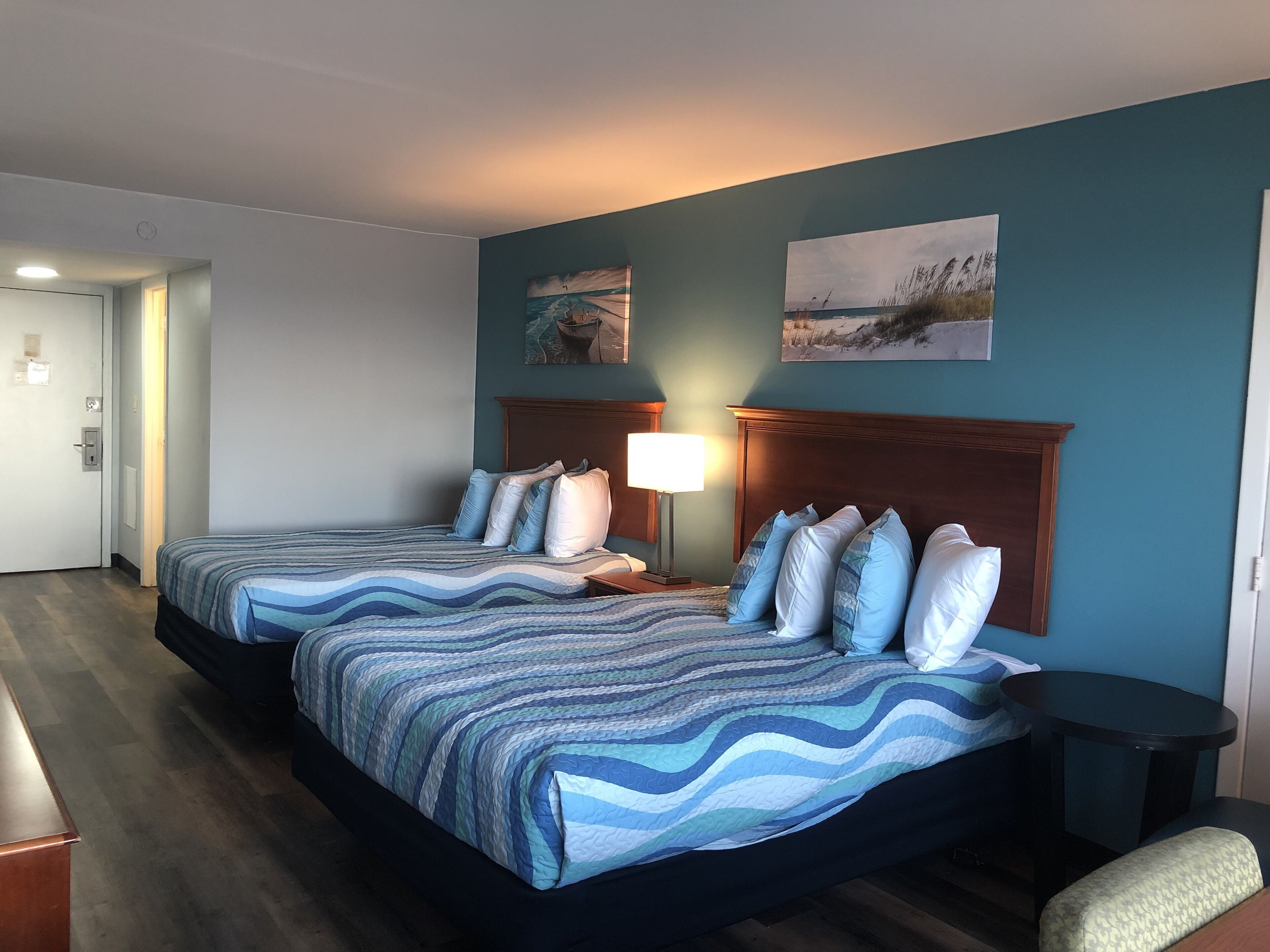 Una camera d'albergo con due letti, un comodino, una lampada e opere d'arte alle pareti.