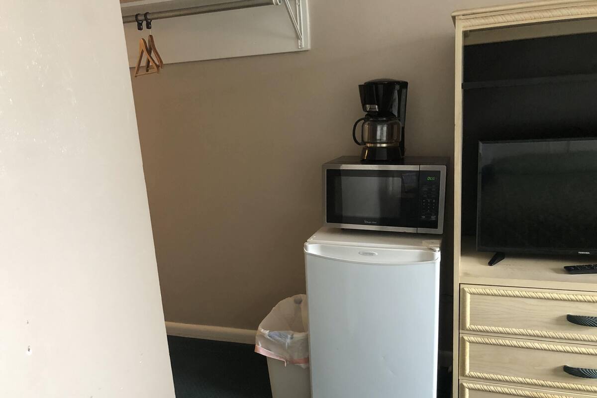 A compact kitchenette with a microwave, coffee maker, refrigerator, and a TV on a cabinet.