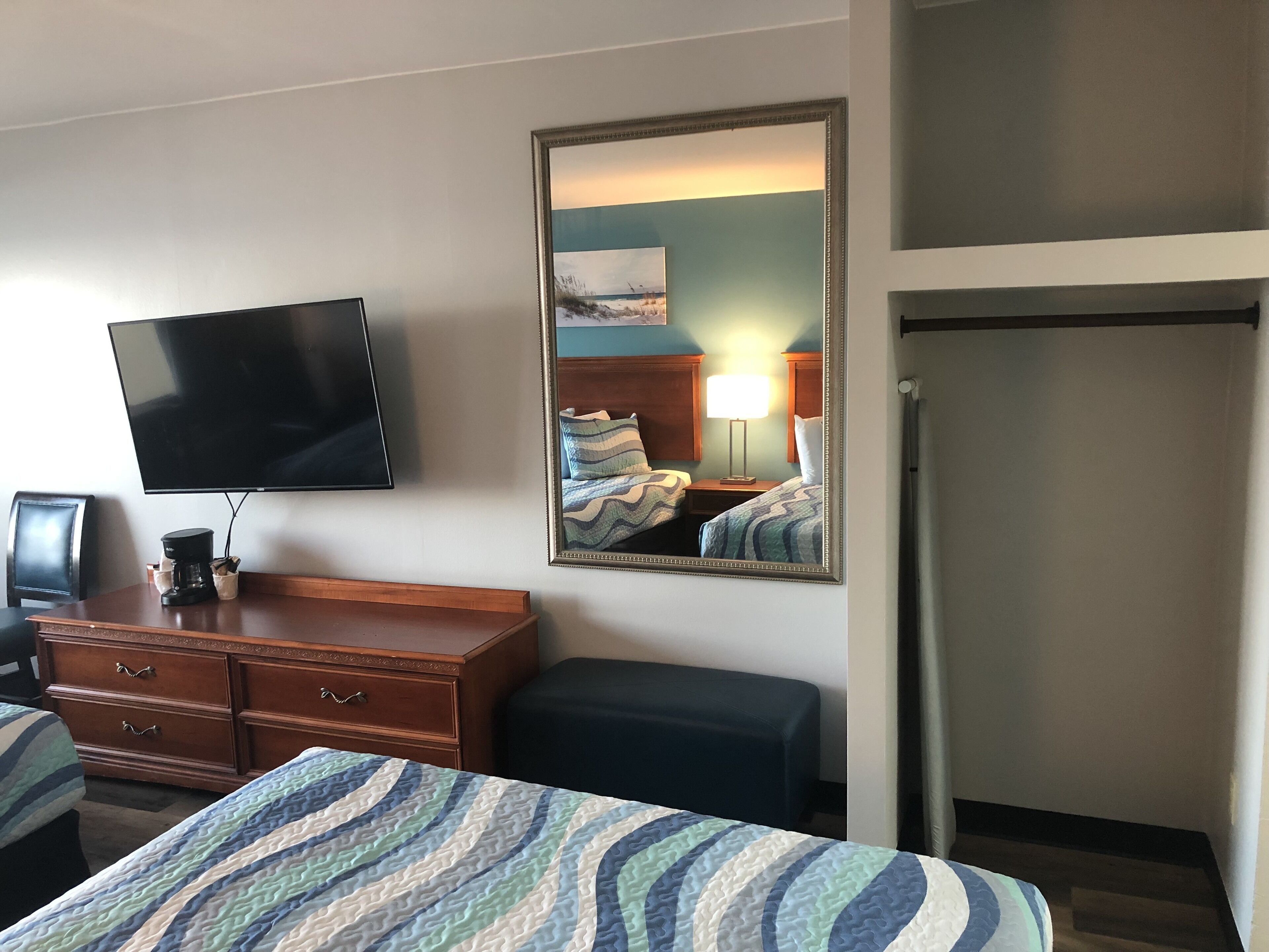 Una habitación de hotel con cama, televisión, cómoda, espejo y puerta.