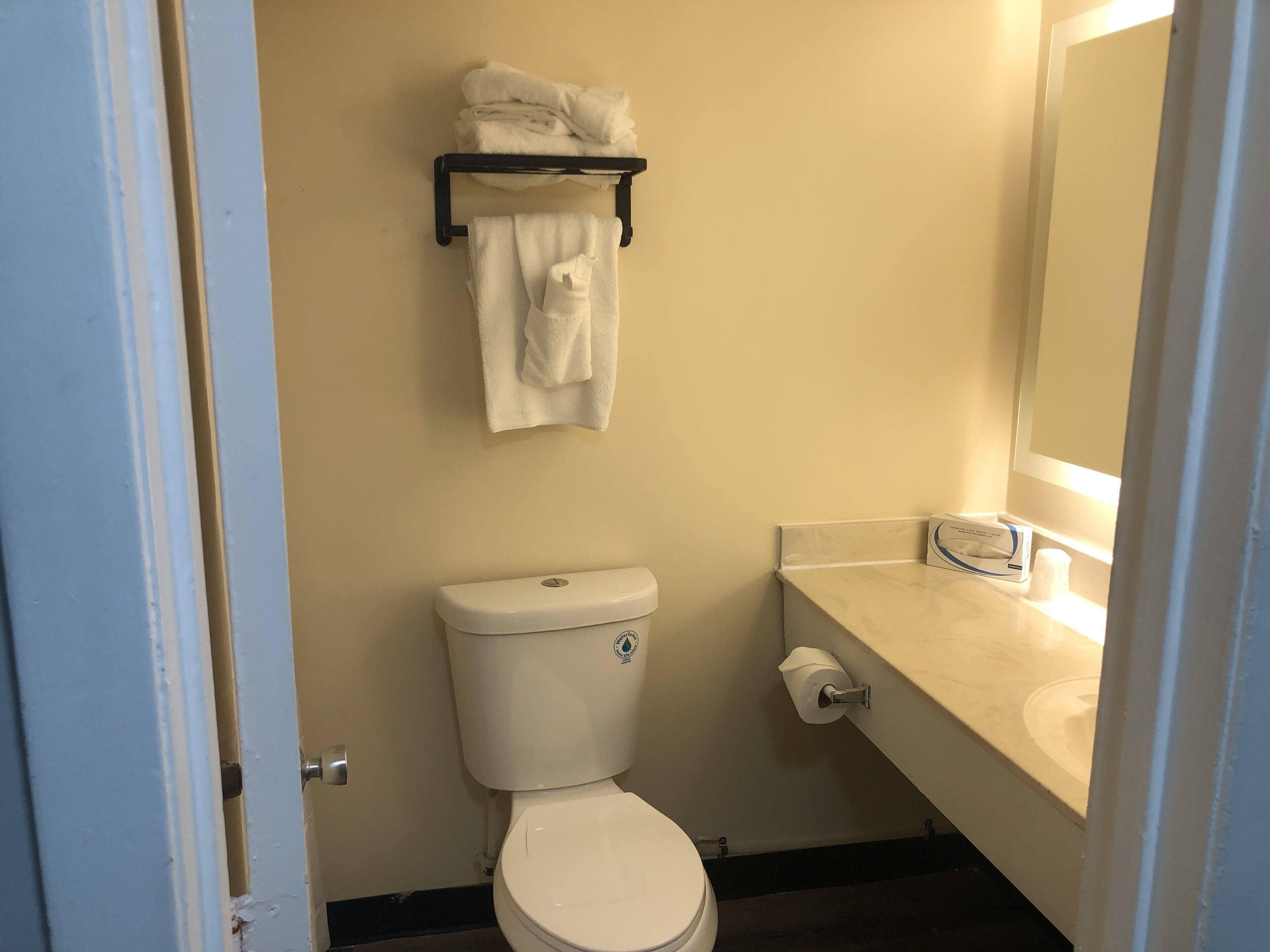 Een compacte badkamer met toilet, een handdoekrek met opgevouwen handdoeken en een wastafel met zeepdispenser.