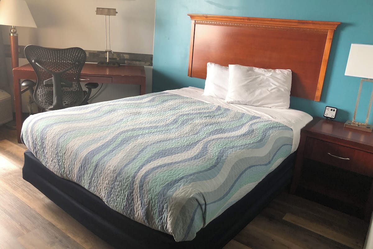 A hotel room with a bed, a desk, a chair, and a nightstand.