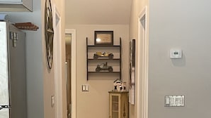 Ein schmaler Flur mit Holzboden, einem Kühlschrank, einer Mülltonne, einem Schrank mit Dekoration und einer Couch.