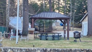Ein Pavillon mit Picknicktischen und Grill in einem Garten mit Teich.