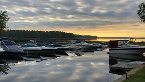 Ein Yachthafen mit mehreren vertäuten Booten, ruhigem Wasser, das den Himmel spiegelt, und einer Rasenfläche mit einer anlegenden Pier.