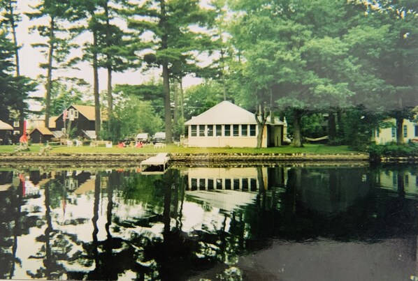 A lakeside building with a reflection in the water, surrounded by trees and other structures. - Lakefront house (Naples)