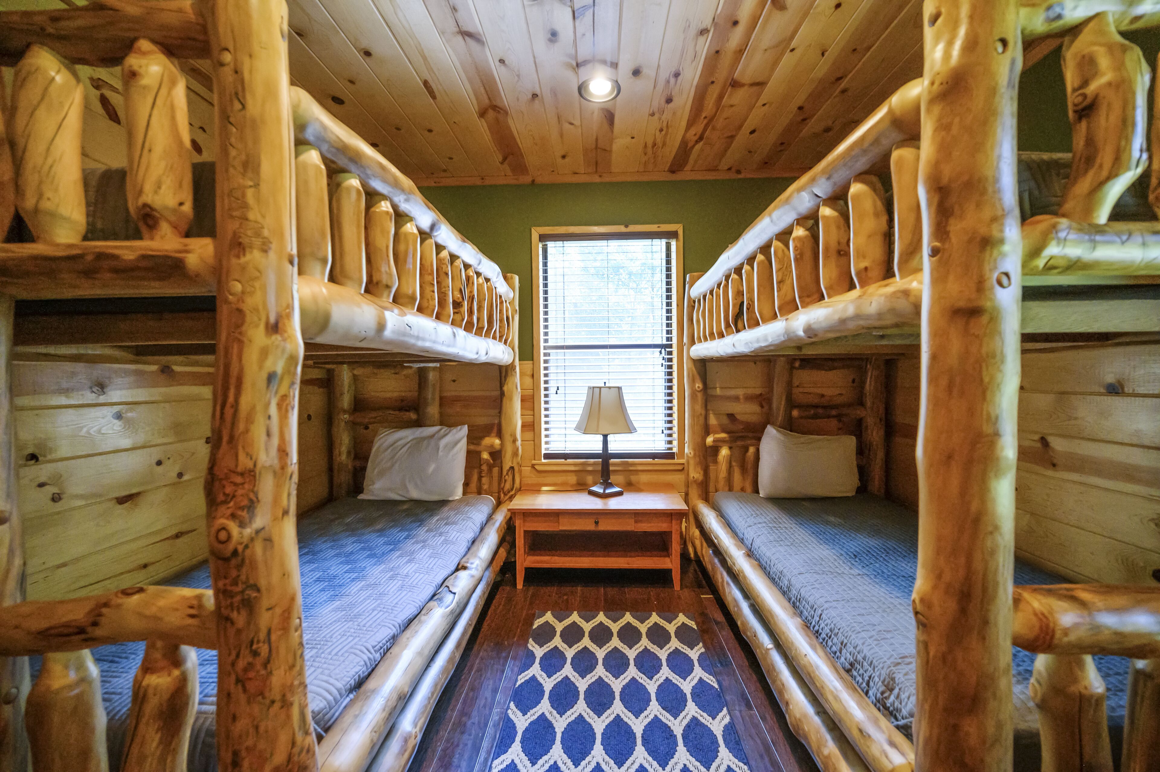 A cabin with bunk beds, a window with blinds, and a small table with a lamp.