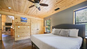 Quarto com uma cama grande, paredes de madeira, ventilador de teto e vista para o exterior.