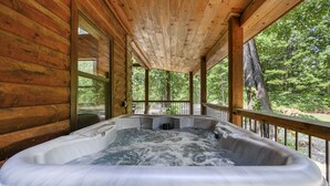 Uma banheira de hidromassagem em uma cabana de madeira com um deck de madeira e vista para a floresta ao redor.