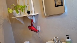 Un baño con inodoro, lavamanos y un secador de pelo en un estante.