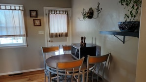 Un área de comedor con una mesa redonda, cuatro sillas, un microondas y una pequeña estantería con objetos decorativos.