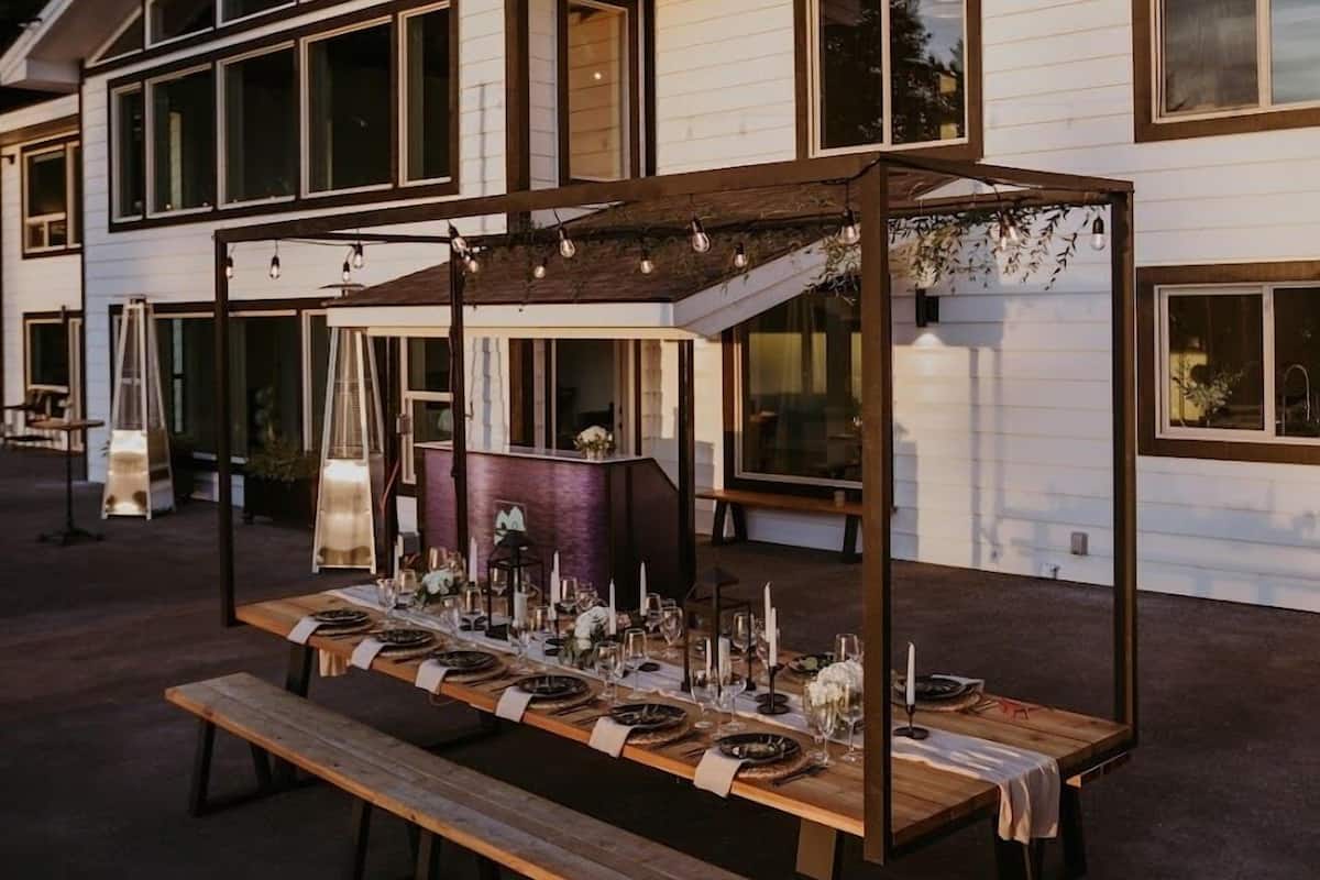 An outdoor dining area with a wooden table set for a meal, surrounded by a pergola structure.