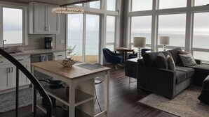 Amplia sala de estar con vista al mar, comedor y cocina con ventanas grandes.