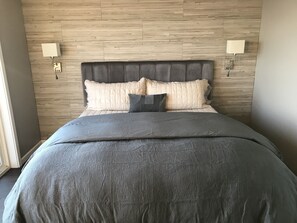 A bedroom with a wooden headboard, a grey bedspread, and two bedside lamps.