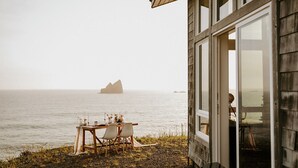 Una cabaña de madera con una mesa preparada para dos, con vista al mar tranquilo y una isla distante.