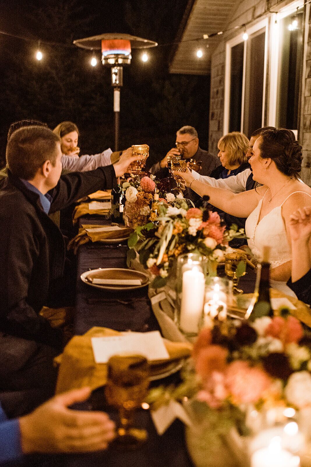 Un grupo de personas brindando alrededor de una mesa de cena con centros de mesa florales y velas.