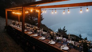 Un área de comedor al aire libre con una pérgola de madera, luces colgantes y vistas al océano.