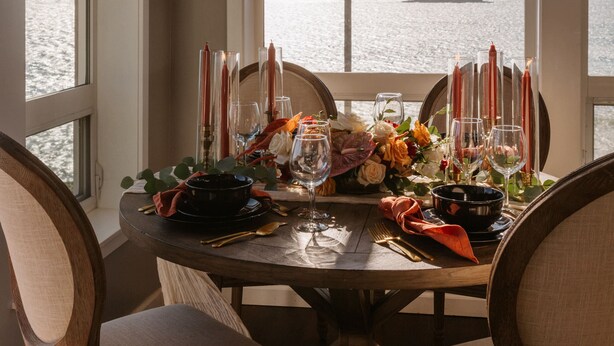 Mesa para dos lista con velas, copas y un arreglo floral, con vista al mar.