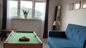A pool table with balls, a blue sofa, a cabinet, a window with a plant, and framed pictures on the wall.