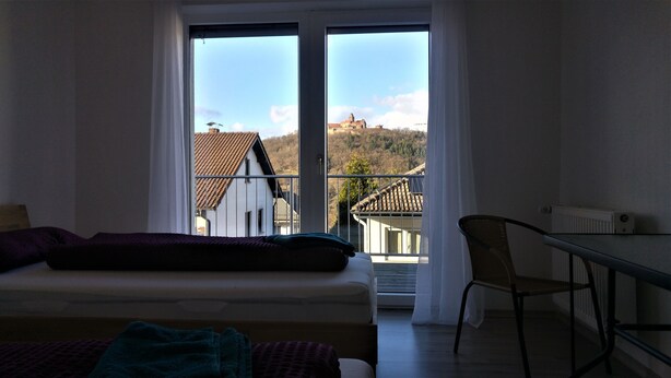 A bedroom with a bed, a chair, and a view of buildings through a window.