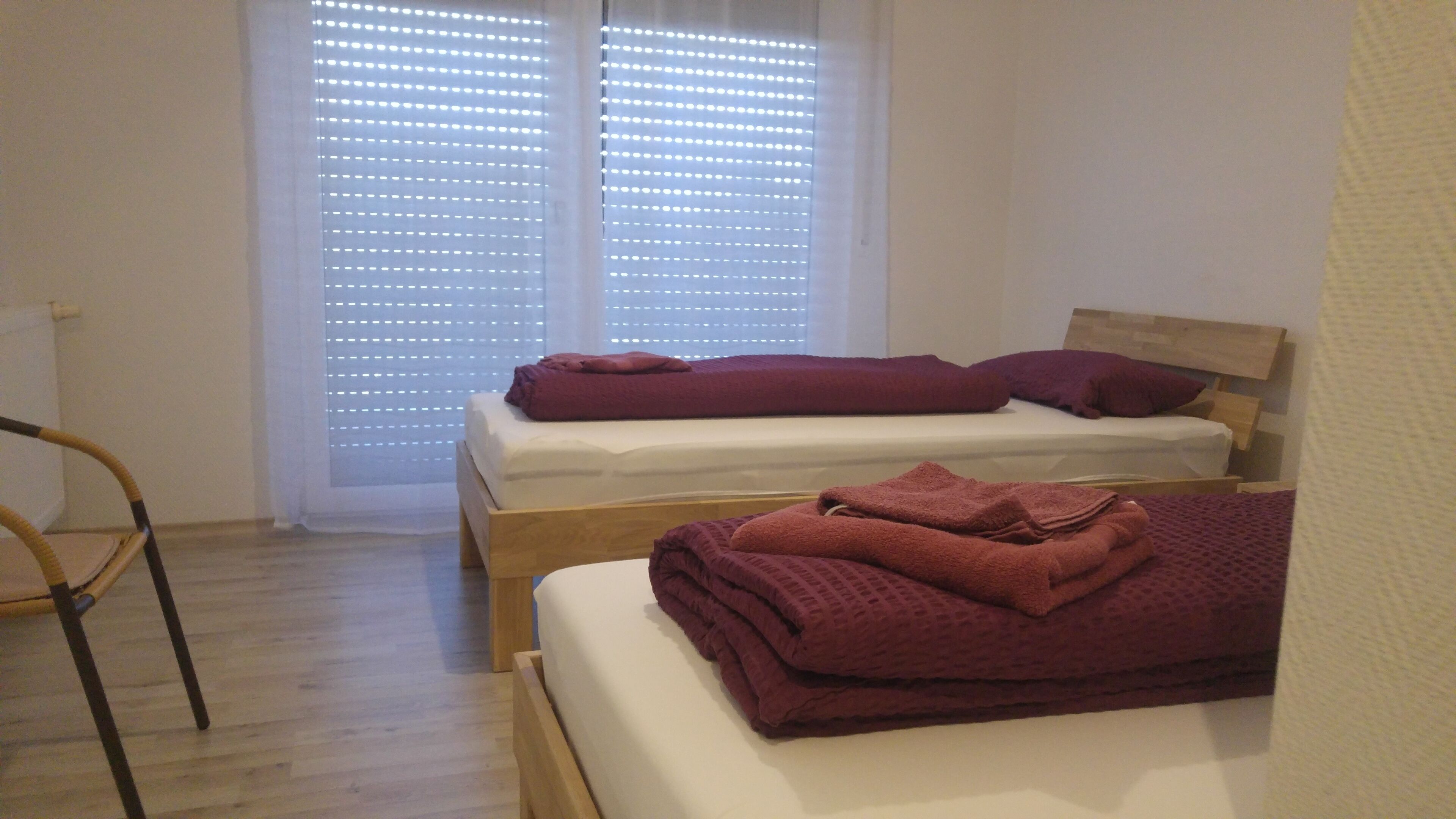 A room with two single beds, a wooden chair, and a window with blinds.