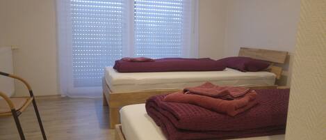 A room with two single beds, a wooden chair, and a window with blinds.
