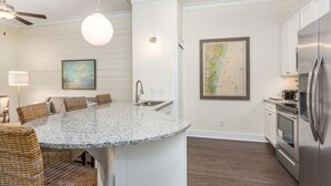 Une cuisine dotée d’un îlot central, d’appareils électroménagers en acier inoxydable et d’un coin repas avec des chaises en osier.
