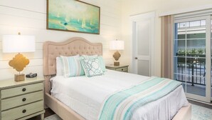 Une chambre à coucher comprenant un lit, deux tables de chevet, une commode, un tableau et une porte-fenêtre coulissante donnant sur un balcon.