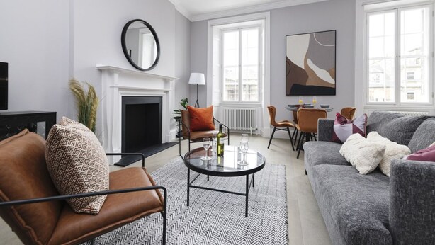 Ein modernes Wohnzimmer mit Kamin, einem runden Tisch mit Gläsern, einer Couch und einem großen, abstrakten Gemälde an der Wand.