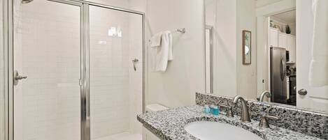 Une salle de bain moderne avec une douche à parois de verre, des toilettes blanches, un lavabo sur un plan de travail en granit et un grand miroir.