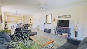 A living room with a sofa, coffee table, and TV. There is a dining area with chairs and a table. The room has a ceiling fan and a large mirror on the wall. - Imagine #2 your vacation at this beautiful condo (Myrtle Beach)