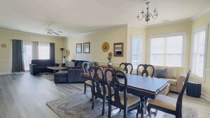 A spacious living room with a dining area, a sofa, a ceiling fan, and a chandelier.