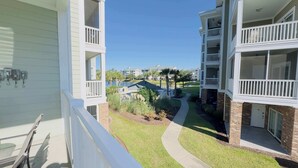 A view from a balcony overlooking a residential area with a pathway leading to a small pond, surrounded by greenery and a clear blue sky. - Imagine #2 your vacation at this beautiful condo (Myrtle Beach)