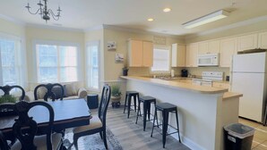 A modern kitchen with white cabinets, a central island, bar stools, and a dining table with chairs. - Imagine #2 your vacation at this beautiful condo (Myrtle Beach)