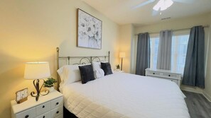A neatly arranged bedroom with a large bed, bedside lamps, a clock, and a window with curtains.