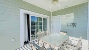 A covered patio with a glass table and chairs, a ceiling fan, and a door with a glass panel.