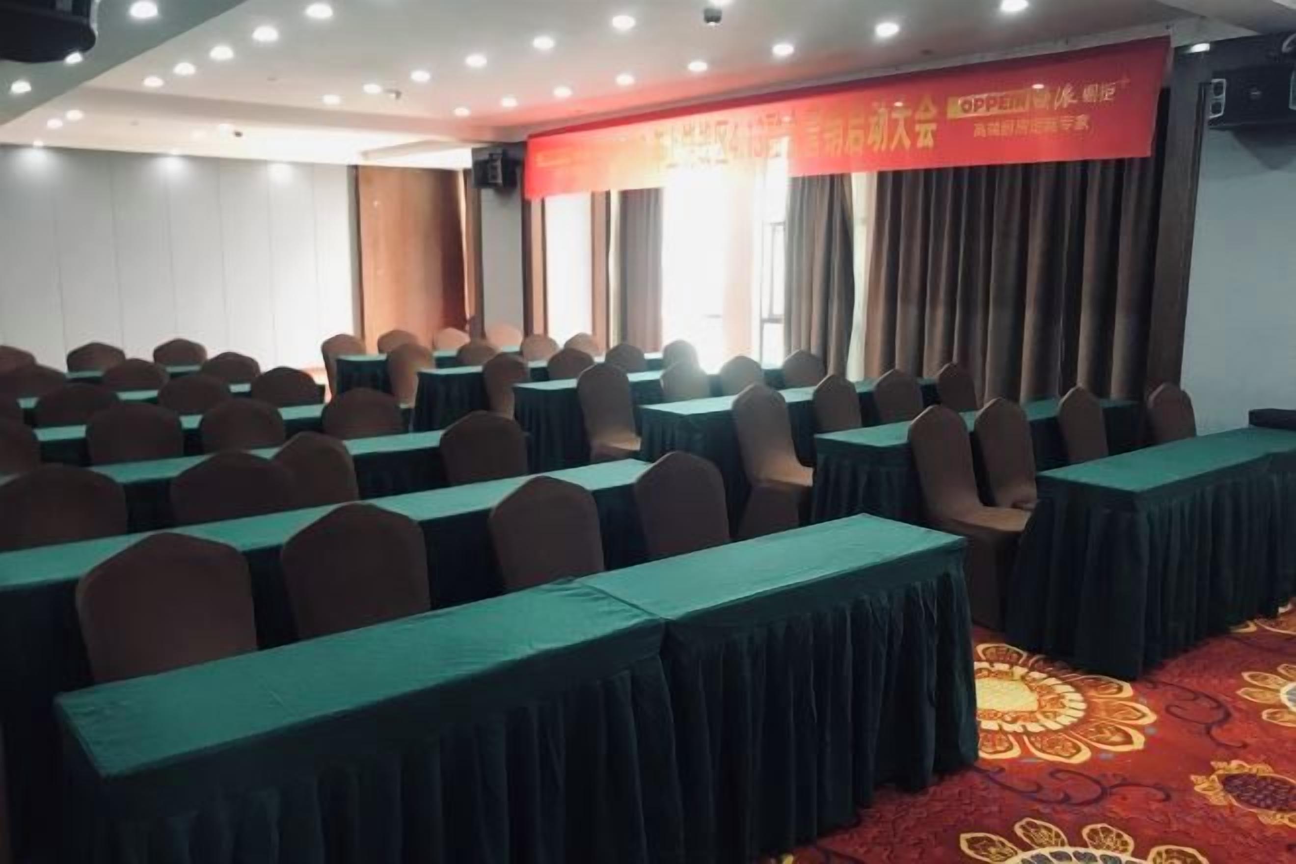 A conference room with rows of tables and chairs, a red carpet, and a banner on the wall.
