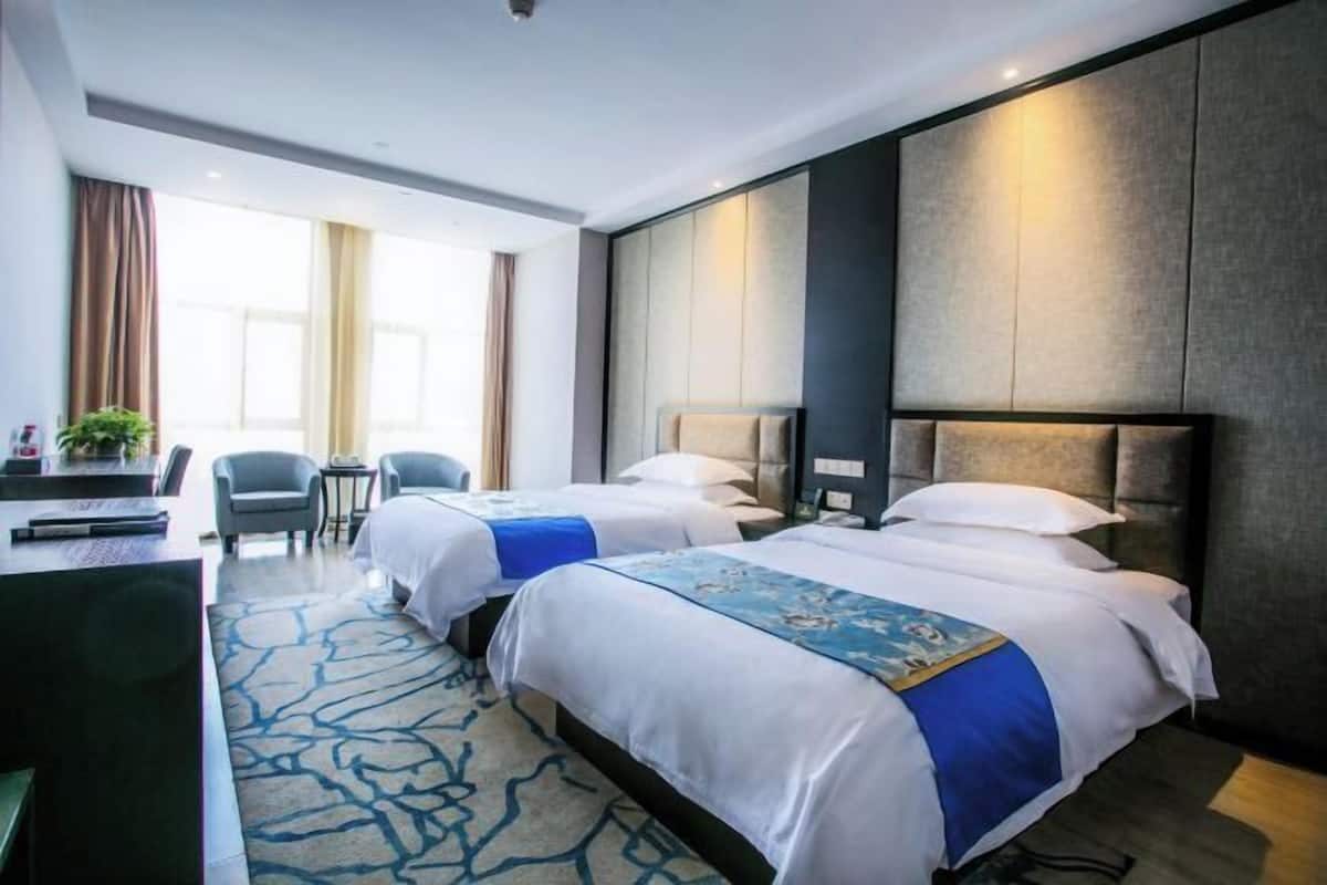 A hotel room with two beds, a desk, a chair, and a large window.