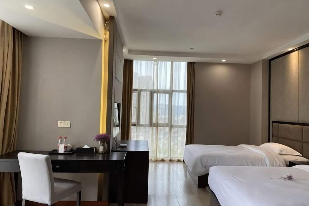 A hotel room with a desk, two beds, a large window, and a view of the city.