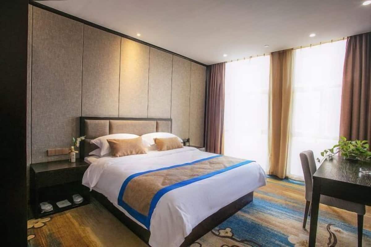 A hotel room with a bed, a nightstand, a chair, a table, and a window with curtains.