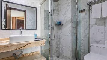 Un baño con lavamanos de mármol, ducha con mampara de vidrio y retrete.