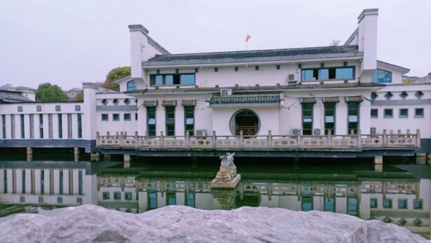 A traditional building with a large central courtyard, a statue in the water, and a flag on top. - Zhongpu Hotel (Shangrao)