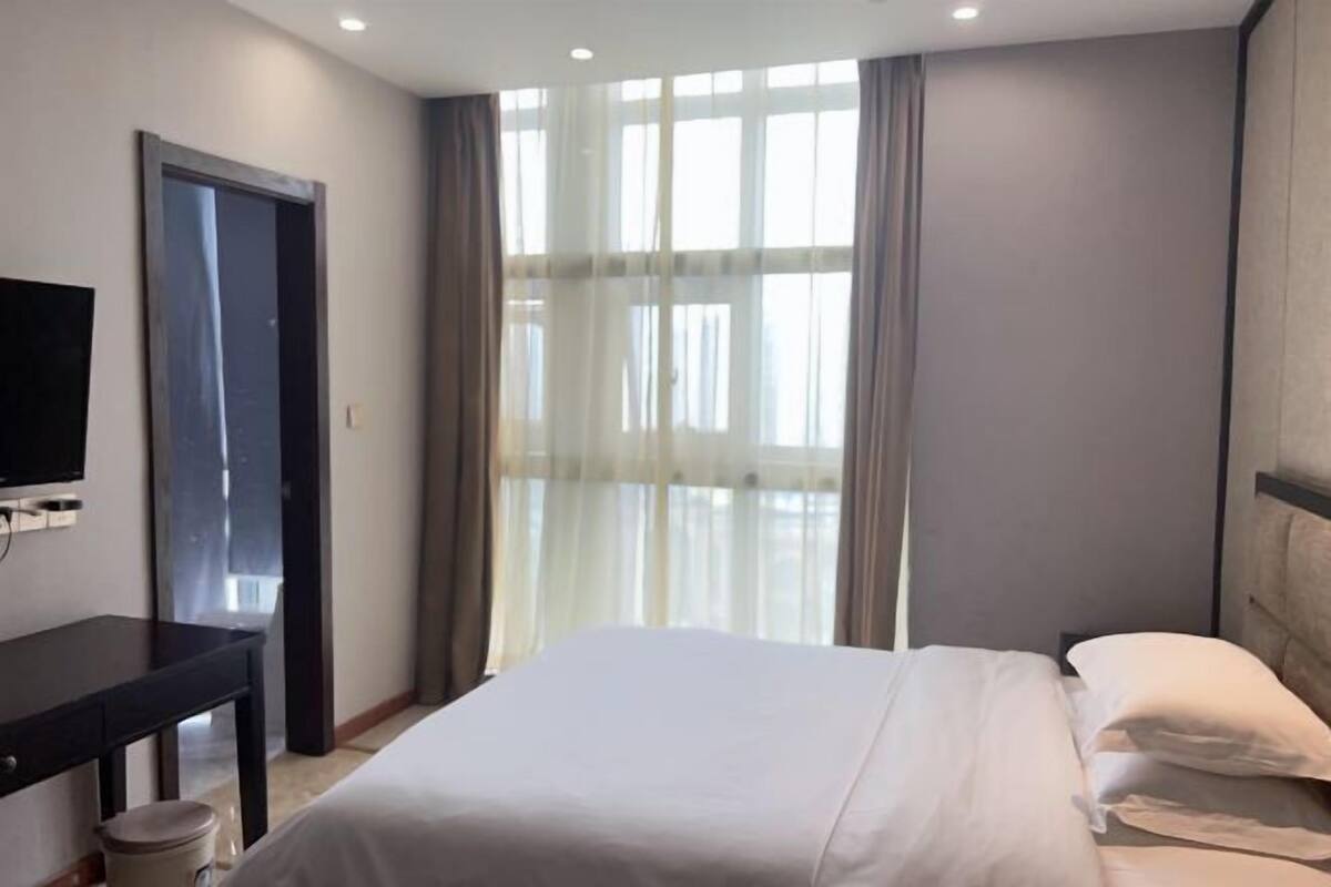 A hotel room with a bed, a desk, a television, and a window with curtains.