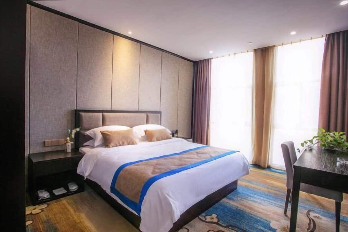 A hotel room with a large bed, a nightstand, a chair, and a window with curtains.
