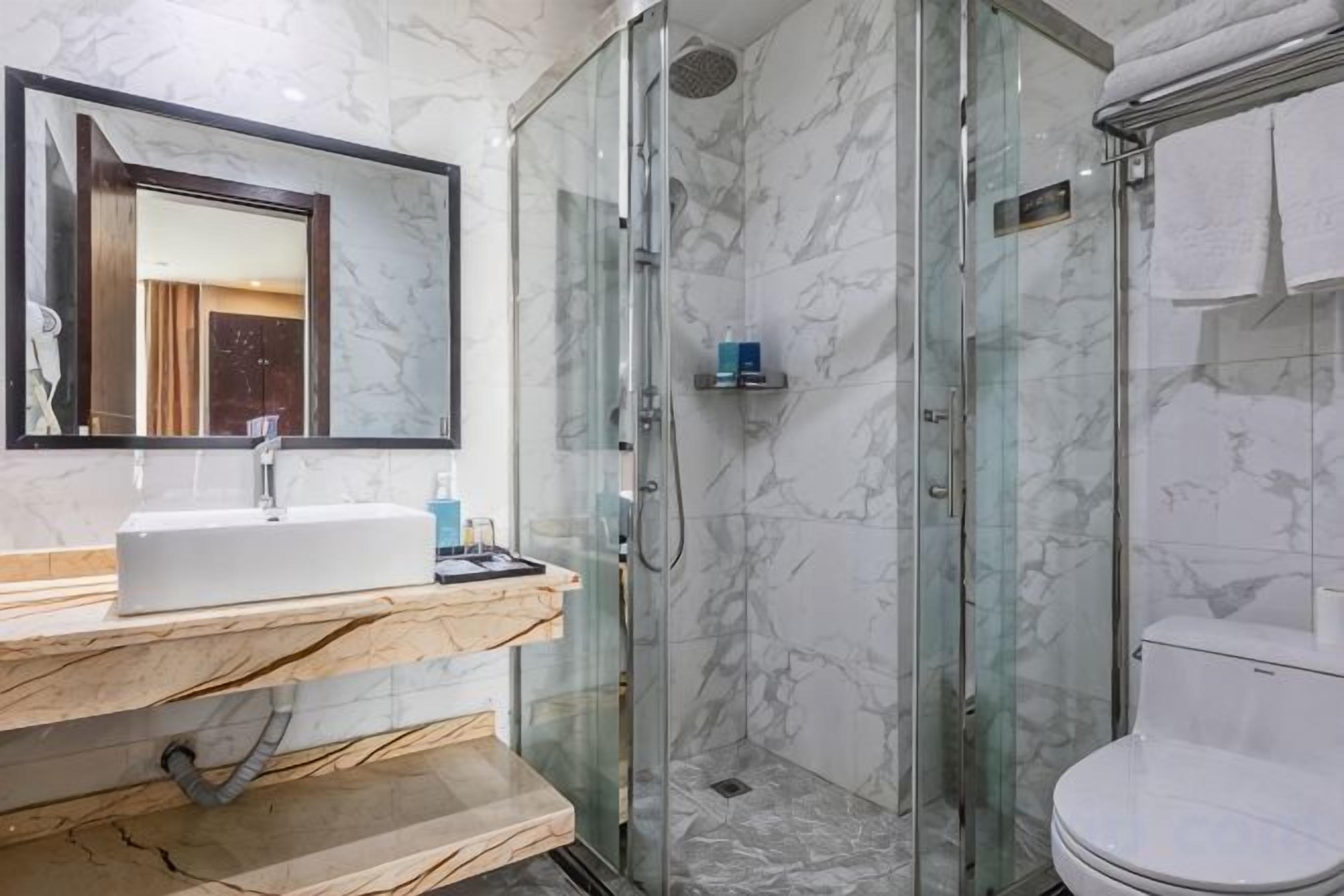 A bathroom with a glass-enclosed shower, a sink with a marble countertop, and a toilet.