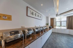 Een buffetgedeelte met verschillende voedseldispensers, een lijst in een kader aan de muur, en een groot raam met gordijnen.